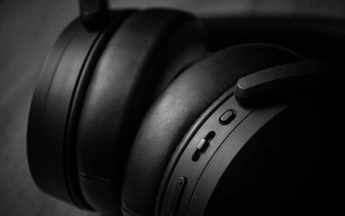 An over-ear headphone photographed close against a dark ground, earcup and hinge in shallow focus.