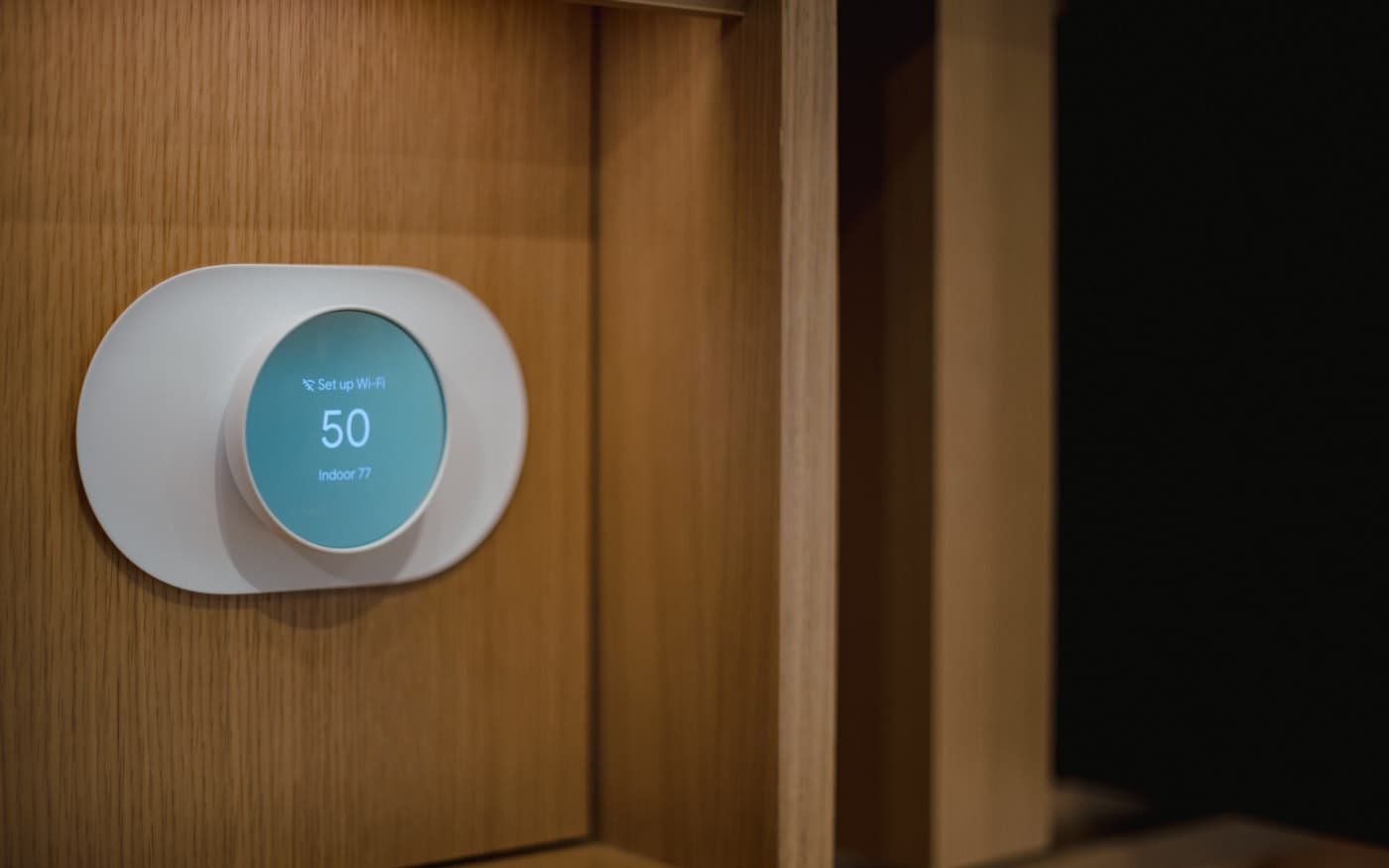 A round wall thermostat on a wooden panel, its display lit.